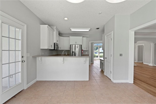 223 Edge Water Dr, Brunswick, GA 31525 - kitchen with stainless steel appliances, a textured ceiling, a peninsula, light tile patterned flooring, and baseboards
