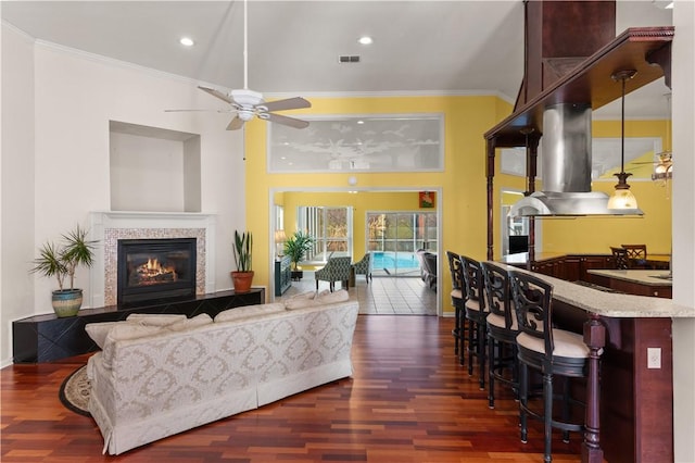 living room featuring ceiling fan, ornamental molding, dark hardwood / wood-style flooring, and a tiled fireplace