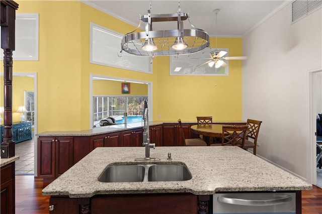 kitchen with light stone counters, ornamental molding, dark hardwood / wood-style floors, and a center island with sink