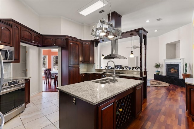 kitchen featuring appliances with stainless steel finishes, hanging light fixtures, light stone counters, a fireplace, and island exhaust hood