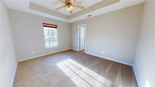 unfurnished room with ceiling fan, a tray ceiling, and light carpet