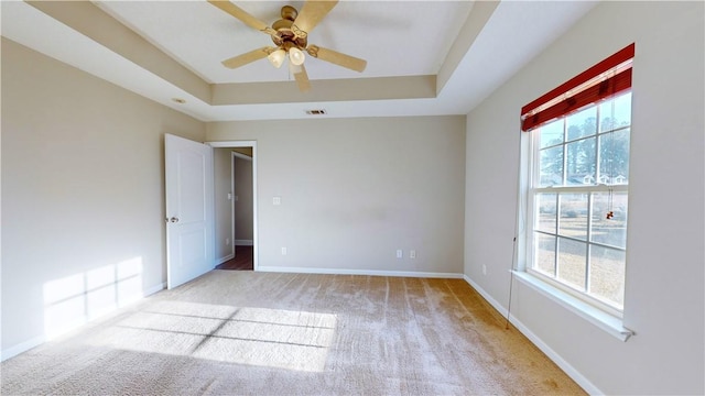 carpeted spare room with ceiling fan and a tray ceiling