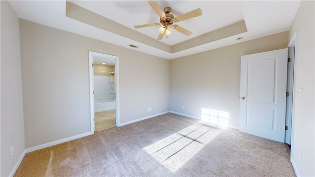 unfurnished bedroom featuring light carpet, ceiling fan, and a tray ceiling