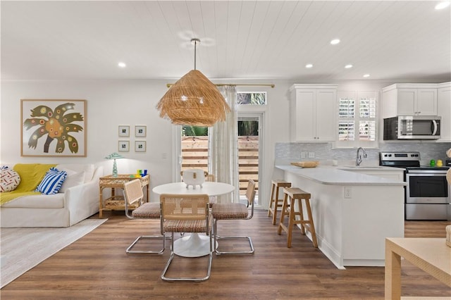 kitchen featuring tasteful backsplash, light countertops, appliances with stainless steel finishes, a kitchen breakfast bar, and dark wood-style flooring