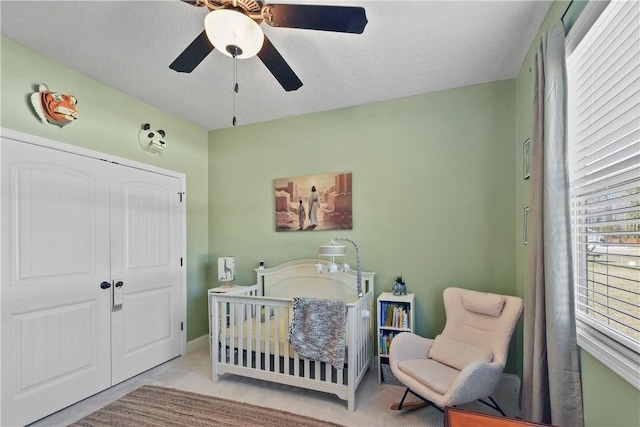 carpeted bedroom with a nursery area, ceiling fan, and a closet