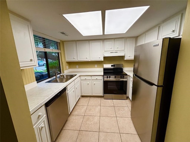 kitchen with stainless steel appliances, under cabinet range hood, a sink, light countertops, and light tile patterned floors