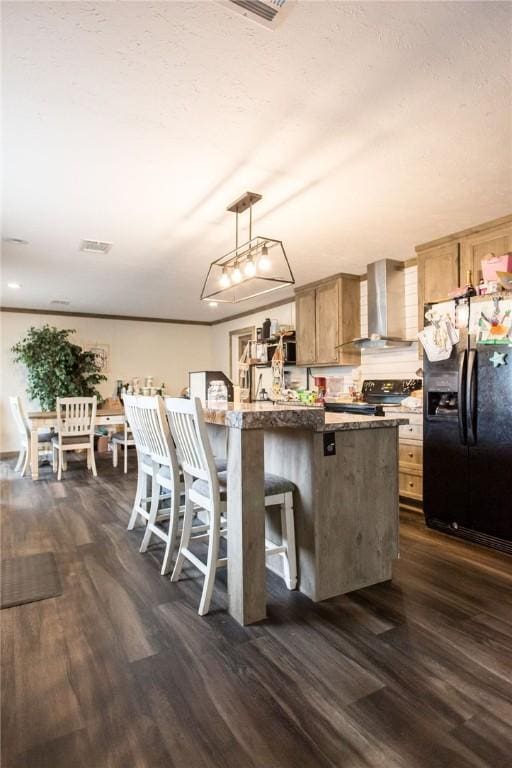 kitchen featuring a breakfast bar, dark wood-style flooring, pendant lighting, black appliances, and wall chimney exhaust hood