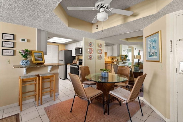 dining area featuring ceiling fan, light tile patterned flooring, and a textured ceiling