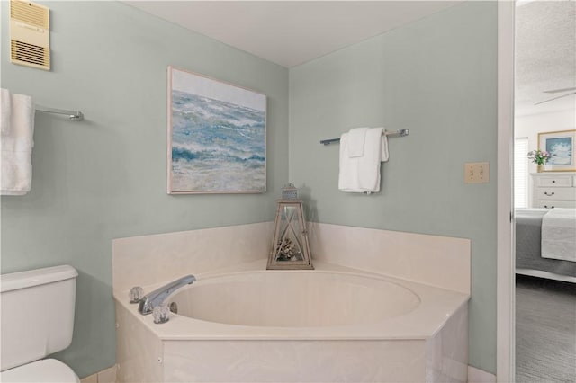 bathroom with a washtub, toilet, and ceiling fan