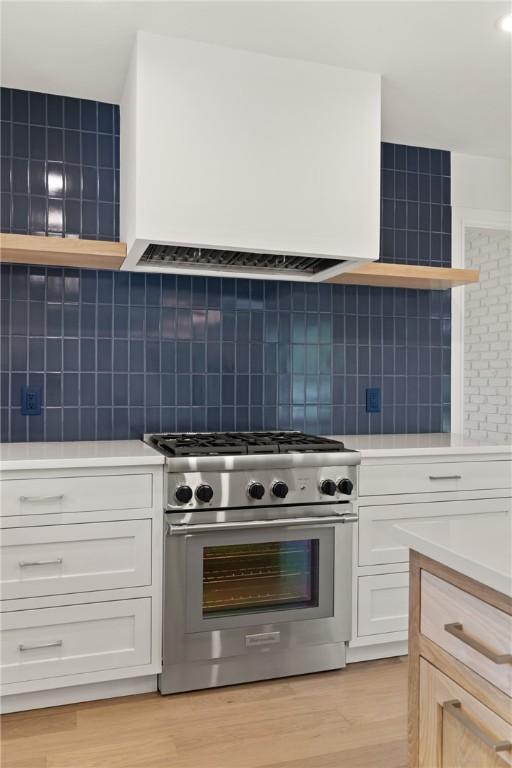 kitchen featuring stainless steel stove, open shelves, light countertops, light wood-type flooring, and white cabinets