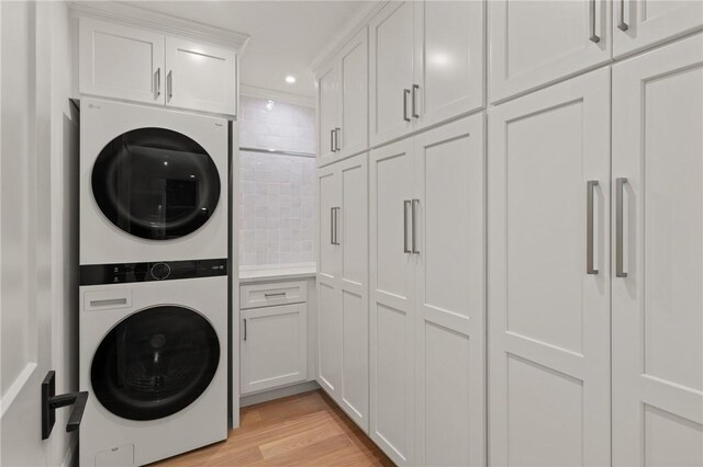 clothes washing area featuring cabinet space, stacked washer and clothes dryer, light wood-style flooring, and recessed lighting