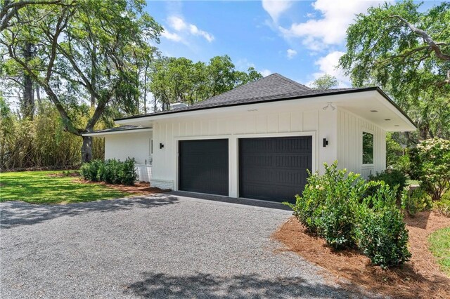 view of side of home featuring an attached garage, gravel driveway, and roof with shingles