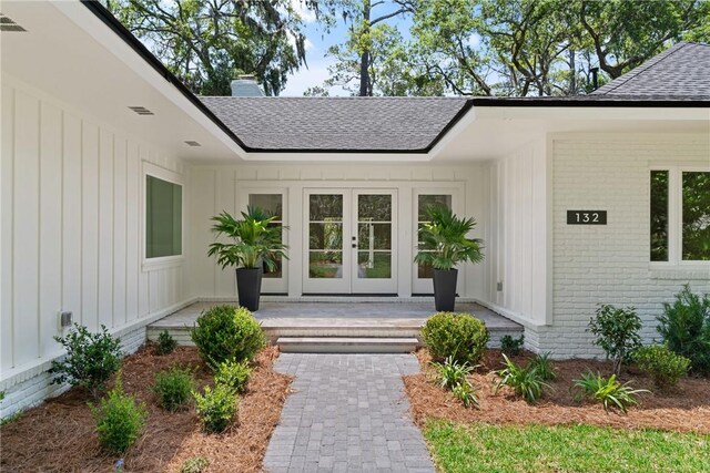 property entrance featuring roof with shingles, board and batten siding, french doors, and brick siding
