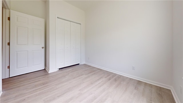 unfurnished bedroom featuring light wood finished floors, baseboards, and a closet