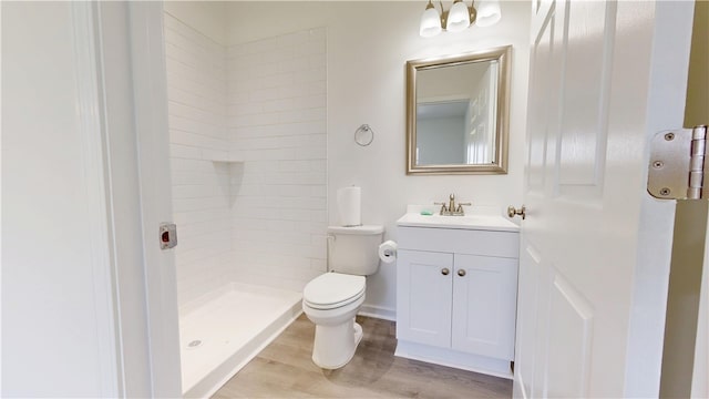bathroom featuring toilet, vanity, tiled shower, and wood finished floors