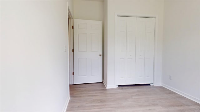 unfurnished bedroom with light wood finished floors, baseboards, and a closet