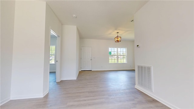 empty room with baseboards, visible vents, light wood-style flooring, and an inviting chandelier