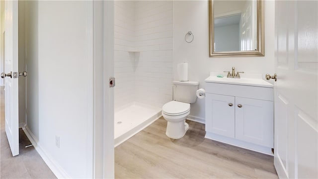 full bath with baseboards, toilet, wood finished floors, tiled shower, and vanity