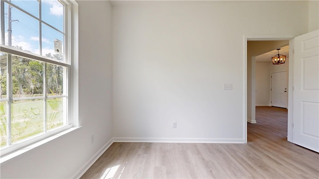 empty room featuring baseboards, a chandelier, and light wood finished floors