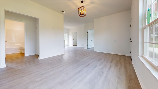 empty room featuring baseboards, visible vents, light wood-style flooring, and a notable chandelier