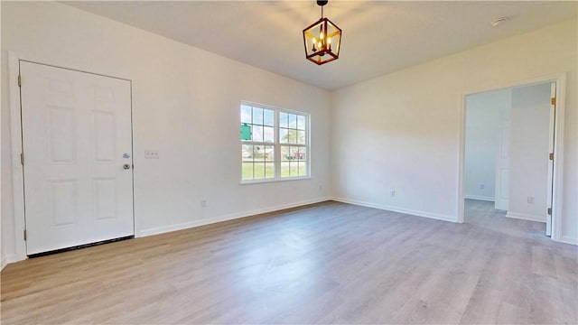 empty room with a notable chandelier, baseboards, and light wood-type flooring
