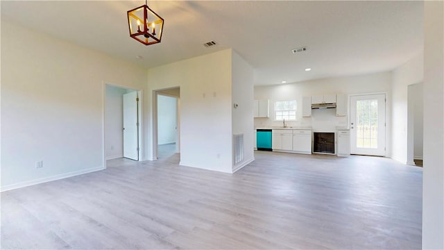 unfurnished living room with visible vents, a sink, a notable chandelier, and light wood finished floors