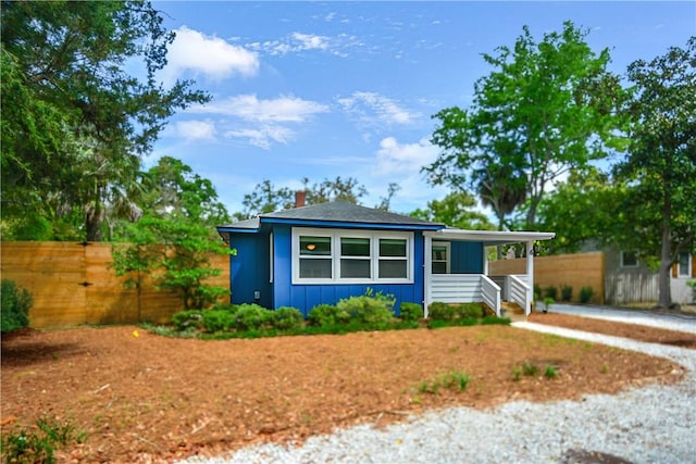 bungalow-style home with board and batten siding, fence, and a chimney
