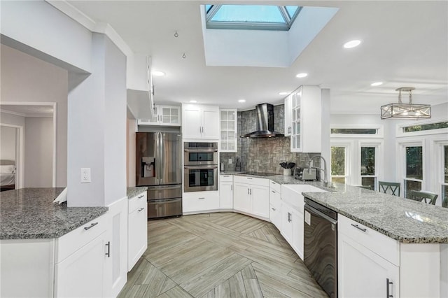 kitchen featuring appliances with stainless steel finishes, white cabinetry, sink, light stone countertops, and wall chimney range hood