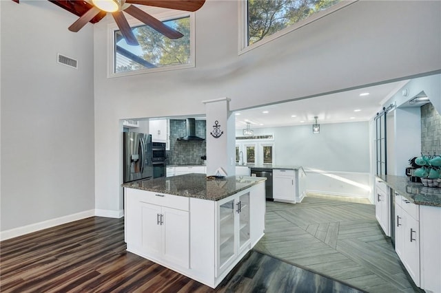 kitchen featuring stainless steel refrigerator with ice dispenser, wall chimney range hood, dishwasher, dark stone counters, and white cabinets