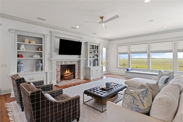 50 Frederica Oaks Ln, Saint Simons Island, GA 31522 - living room with a brick fireplace, crown molding, a ceiling fan, built in features, and wood finished floors