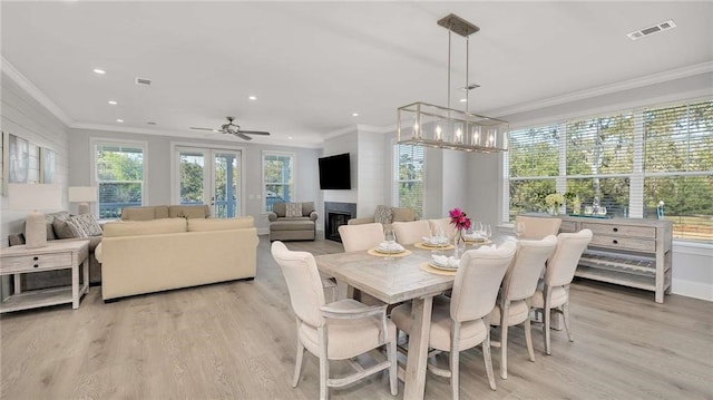 dining space with ornamental molding, a glass covered fireplace, light wood-type flooring, and visible vents