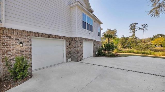 view of side of home with driveway, an attached garage, and brick siding