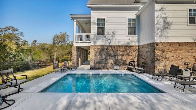 back of house with a fenced in pool, a patio, a balcony, fence, and brick siding