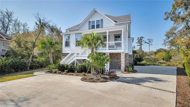 coastal inspired home featuring stairs, a porch, concrete driveway, and brick siding