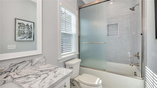 bathroom with shower / bath combination with glass door, vanity, toilet, and a healthy amount of sunlight