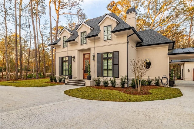 view of front of property with stucco siding, concrete driveway, a chimney, and a shingled roof