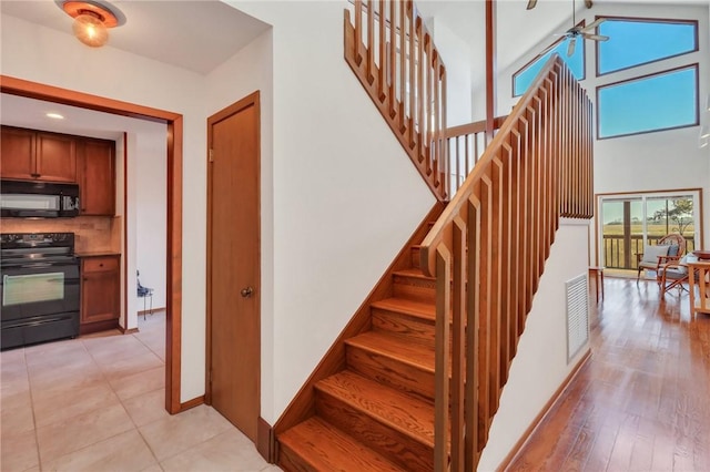 stairs featuring hardwood / wood-style floors, high vaulted ceiling, and ceiling fan