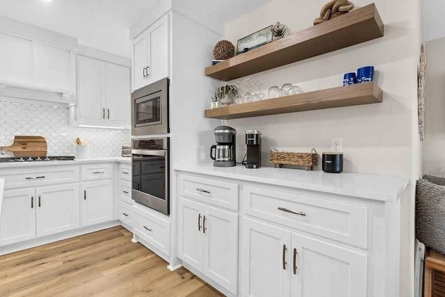 kitchen featuring backsplash, light hardwood / wood-style flooring, white cabinets, and appliances with stainless steel finishes