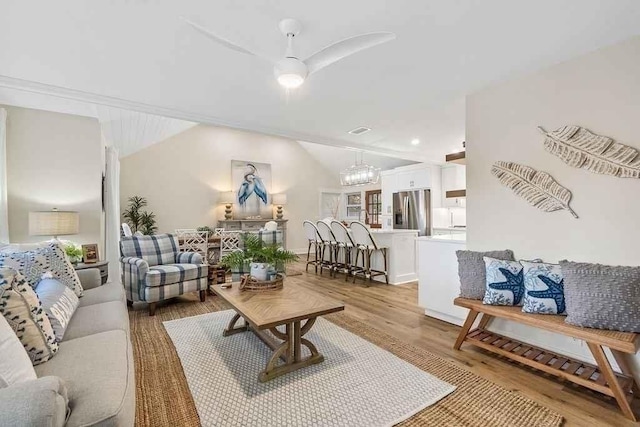 living room featuring ceiling fan with notable chandelier, light hardwood / wood-style floors, and vaulted ceiling