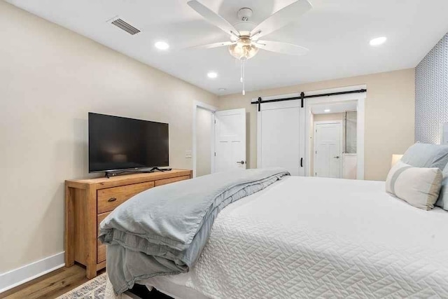 bedroom featuring ceiling fan, a barn door, and wood-type flooring