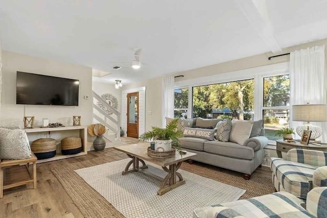 living room with beamed ceiling, ceiling fan, and light wood-type flooring