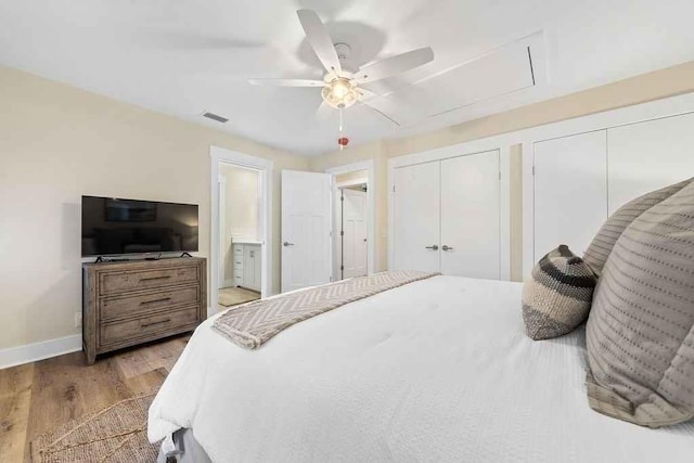 bedroom with ceiling fan, ensuite bathroom, two closets, and hardwood / wood-style flooring