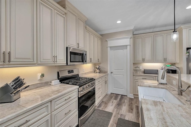 kitchen featuring sink, stainless steel appliances, light hardwood / wood-style floors, decorative light fixtures, and cream cabinetry