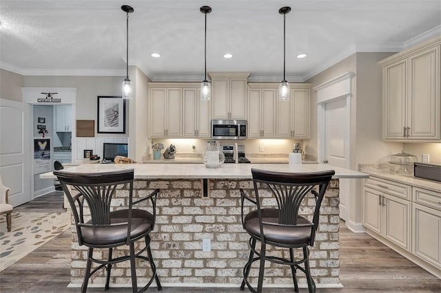 kitchen with a kitchen island with sink, cream cabinets, hardwood / wood-style flooring, decorative light fixtures, and a breakfast bar area