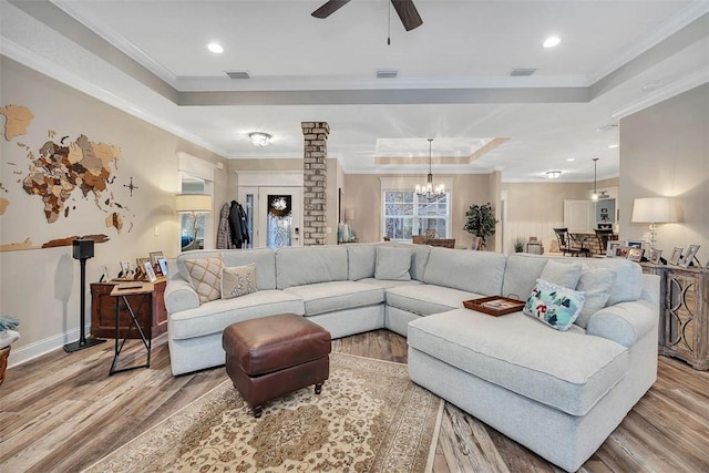 living room featuring ceiling fan with notable chandelier, light hardwood / wood-style floors, ornamental molding, and a tray ceiling