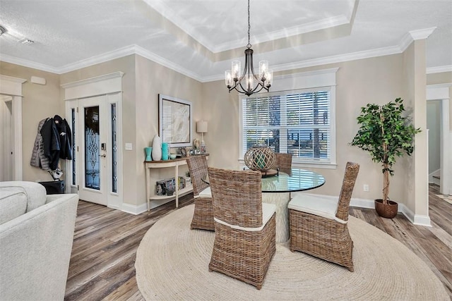 dining area with a notable chandelier, a raised ceiling, wood-type flooring, and ornamental molding