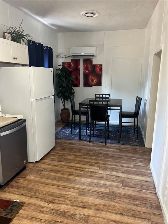 kitchen with appliances with stainless steel finishes, hardwood / wood-style flooring, white cabinetry, and a wall mounted AC