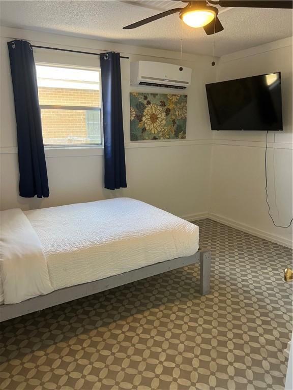 bedroom featuring a textured ceiling, a wall mounted AC, and ceiling fan