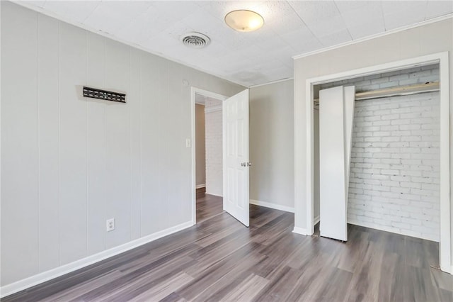 unfurnished bedroom featuring a closet, dark wood-type flooring, and brick wall