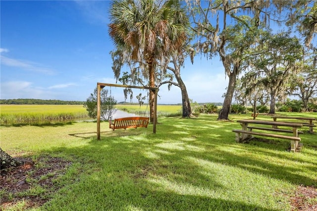 view of property's community with a rural view, a lawn, and a water view